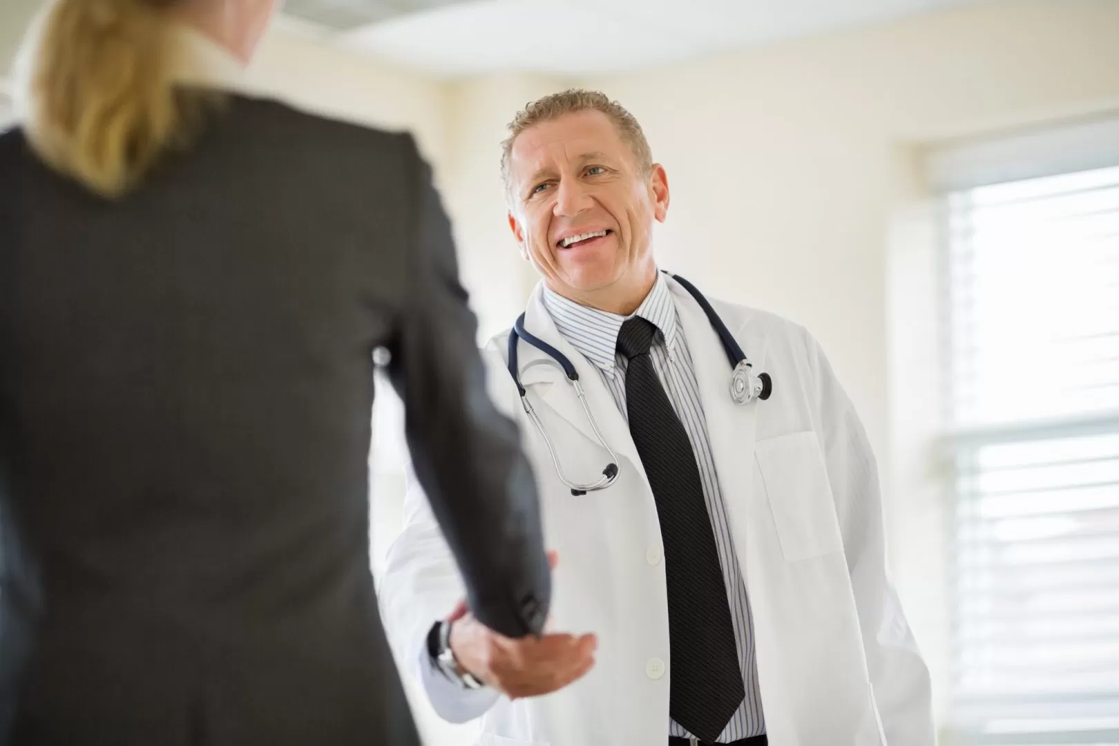 Male doctor cheerfully shaking hands with a businesswoman.