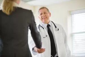 Male doctor cheerfully shaking hands with a businesswoman.