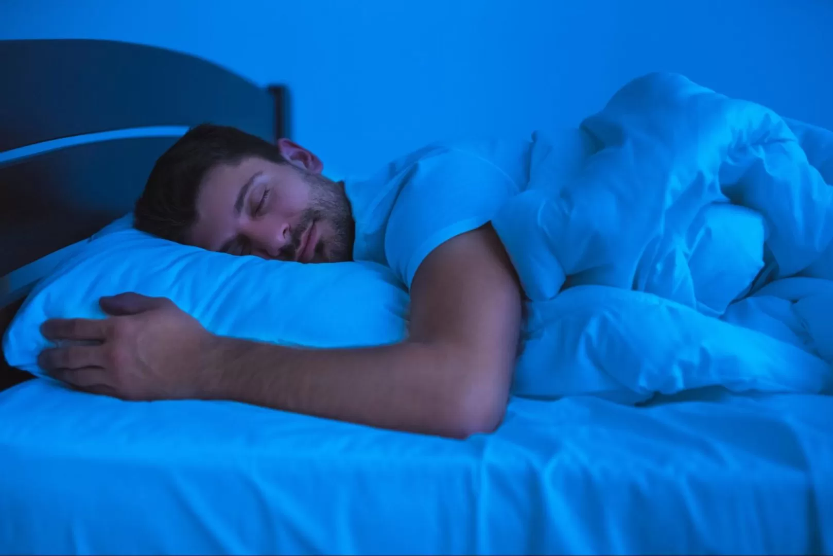 A man comfortably sleeping in bed at nighttime.