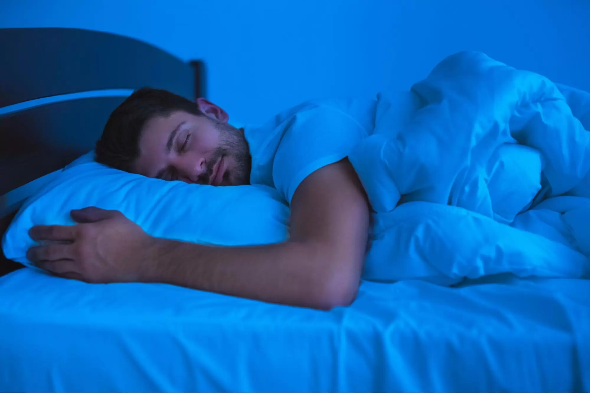 A man comfortably sleeping in bed at nighttime.